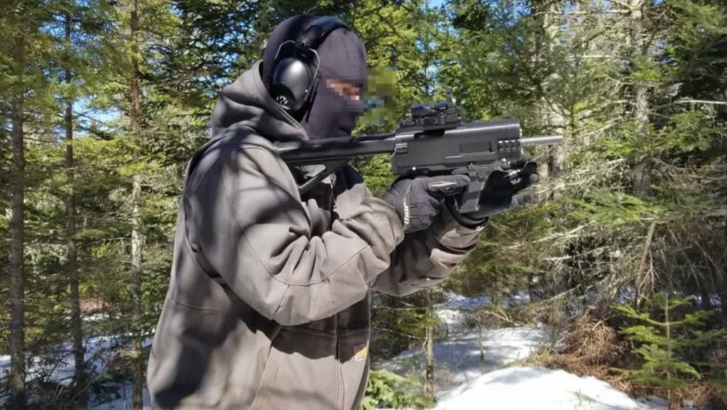 Auf dem Foto ist eine vermummte Person mit Gehörschutz und Handschuhen zu sehen, die in einem verschneiten Wald eine 3D-gedruckte Schusswaffe („Ghost Gun“) im Anschlag hält. Foto: JStark1809 / Deterrence Dispensed (CC BY 4.0)
