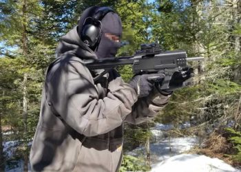 Auf dem Foto ist eine vermummte Person mit Gehörschutz und Handschuhen zu sehen, die in einem verschneiten Wald eine 3D-gedruckte Schusswaffe („Ghost Gun“) im Anschlag hält. Foto: JStark1809 / Deterrence Dispensed (CC BY 4.0)