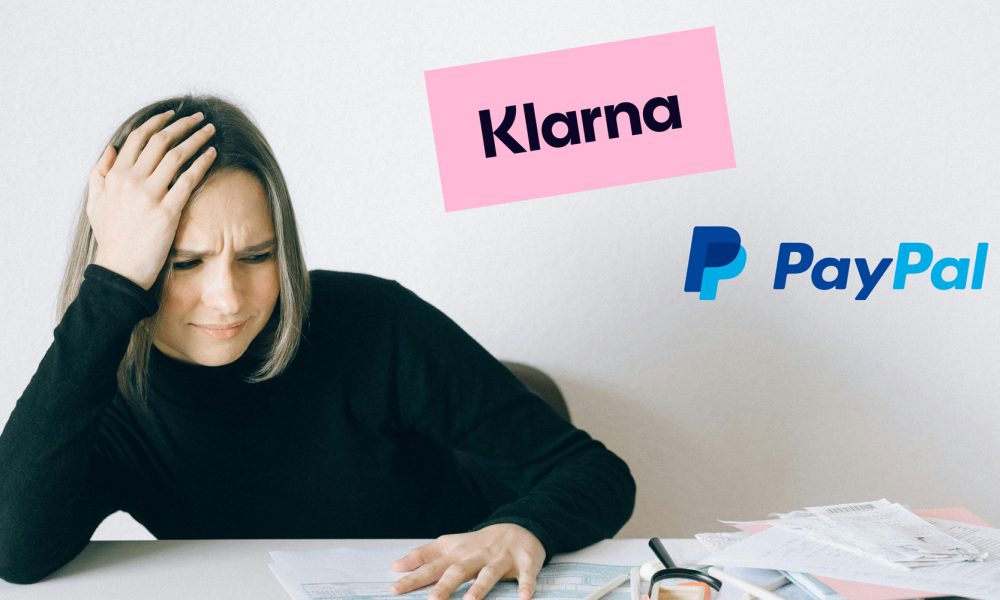 Frau sitzt am Tisch und hält sich mit genervtem Gesichtsausdruck den Kopf, vor ihr liegen Rechnungen und Papierkram. Logos von Klarna und PayPal